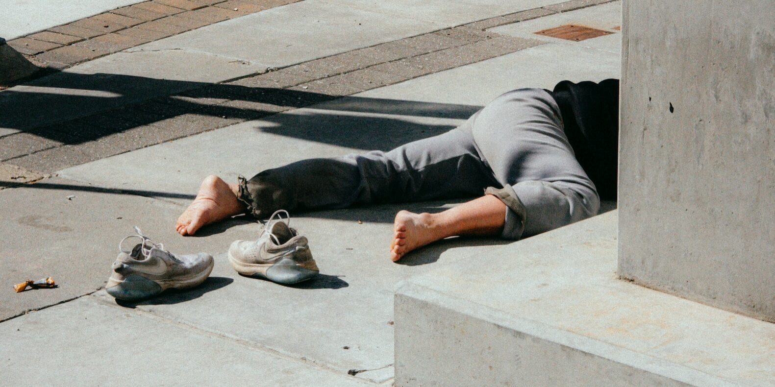 Person in grauer Hose und grauen Schuhen, die auf einer Betonbank sitzt