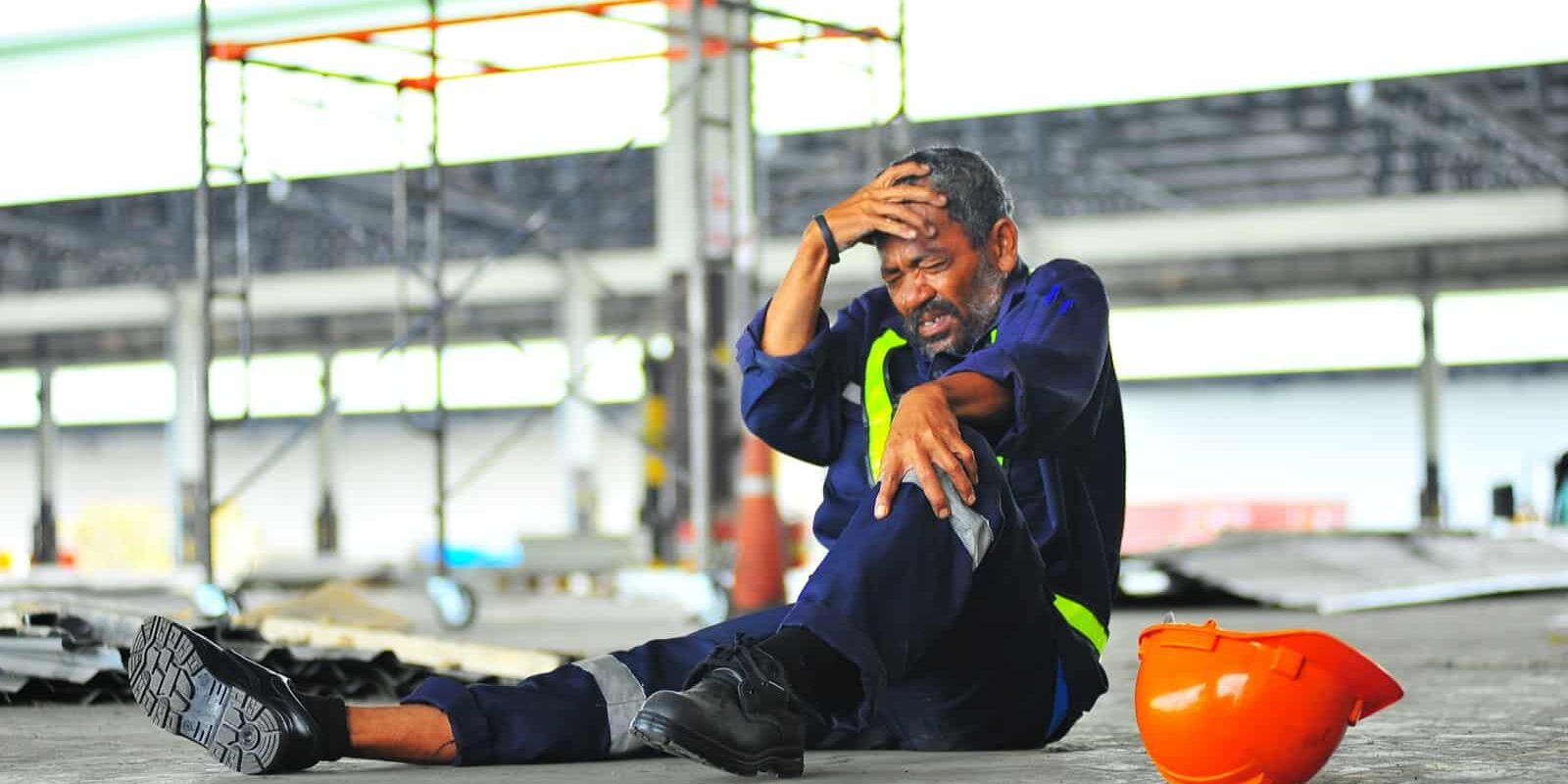 Accident de travailleur senior, chute de l'échafaudage et maux de tête avec jambe cassée dans le concept d'assurance maladie sur chantier.